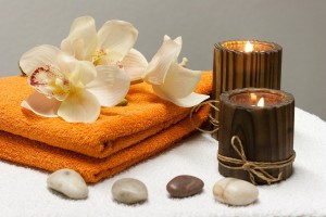 Orange towels with white loitus flowers on top. Two lit candels on the right.